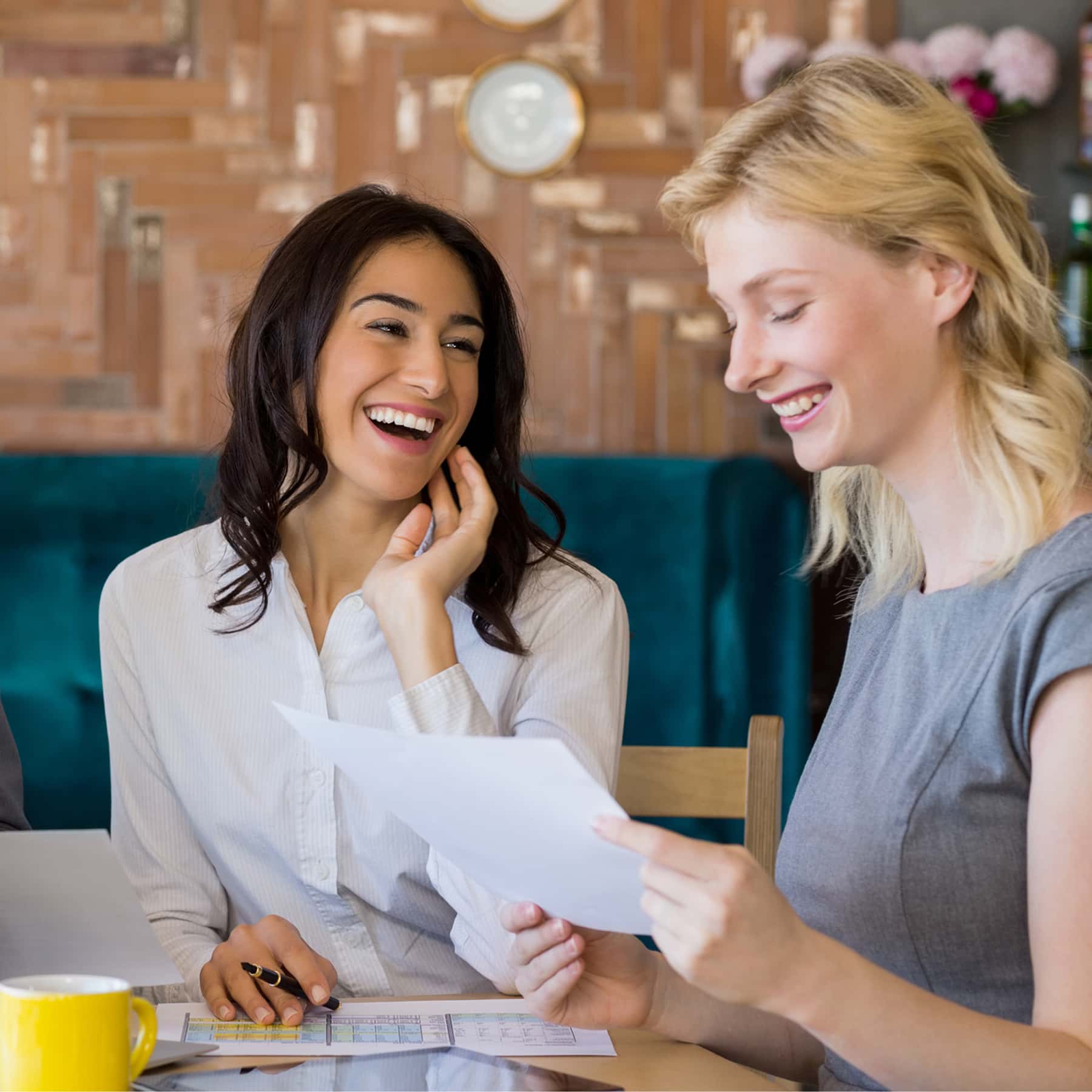 Two insurance professionals meeting with a client at a conference table while reviewing employee benefits plan information and coverage options on printed documents and a laptop.