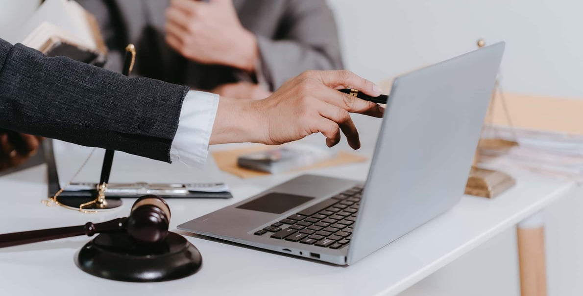 Hand pointing at laptop with a gavel sitting on the desk next to it.